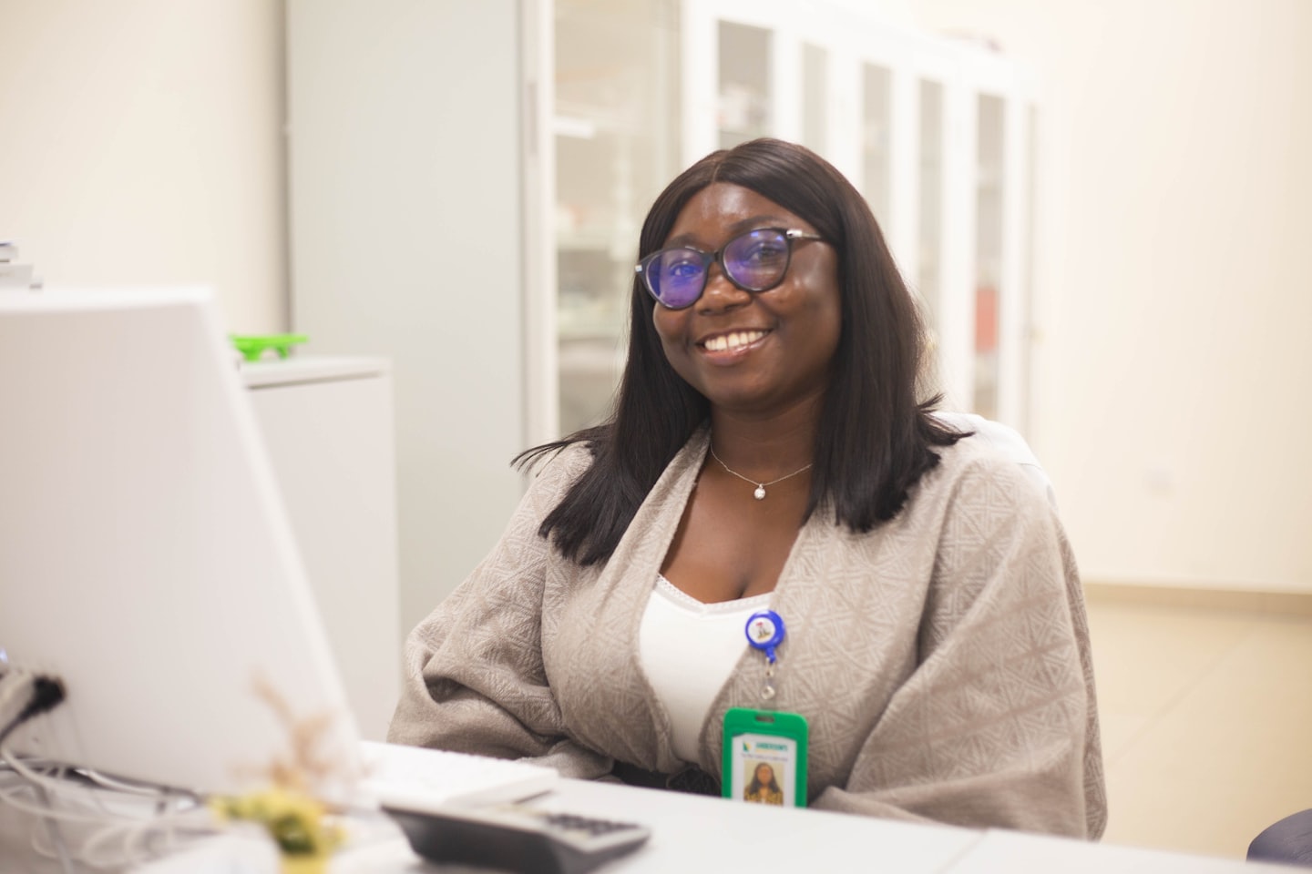 A smiling young woman with glasses at her office desk.